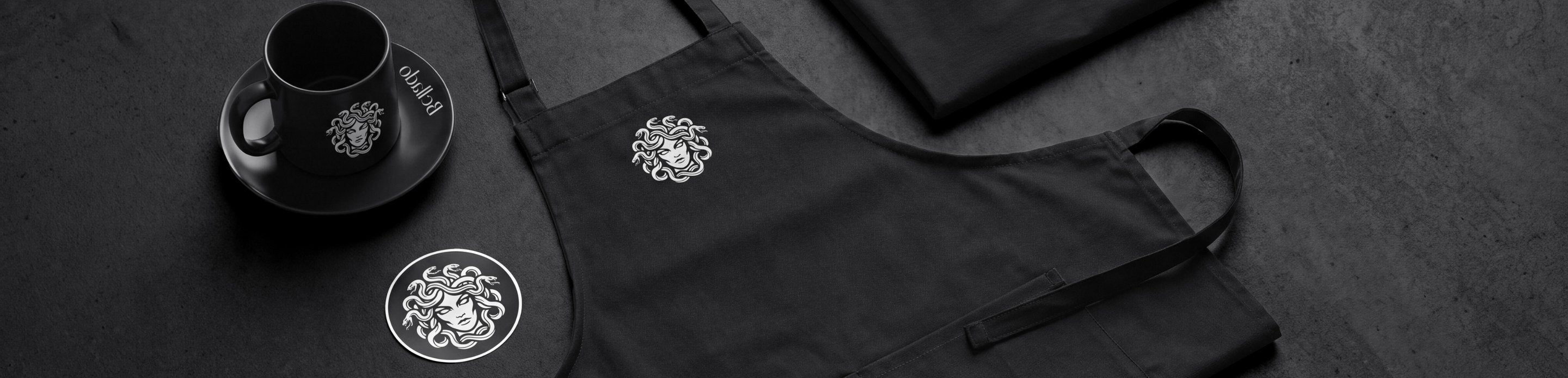 Bellado Merchandise: Schürze, T-Shirt und Espressotasse auf dunklem Stein